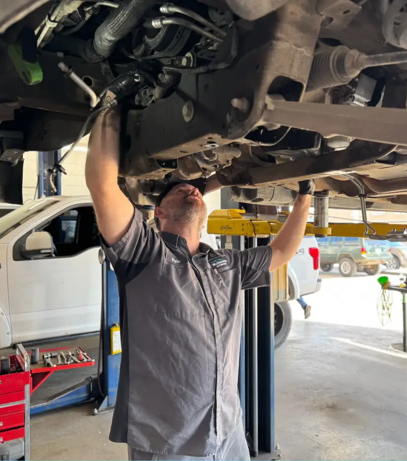 A mechanic, part of the careers at Miller Brothers Automotive, works diligently underneath a lifted vehicle, performing auto repair in Tecumseh, OK.