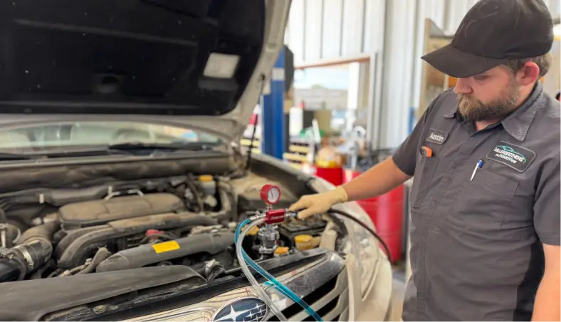 A mechanic at Miller Brothers Automotive performs detailed auto a/c repair under a lifted hood, also specializing comprehensive auto repair in Tecumseh, OK.