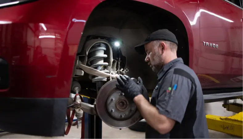 A mechanic at Miller Brothers Automotive inspects the exposed brake system of a red TRAILBLAZER, performing thorough brake repair for auto repair in Tecumseh, OK.