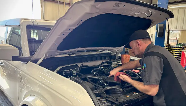 A mechanic performs oil change services under the hood of a white SUV at Miller Brothers Automotive, a trusted spot for auto repair in Tecumseh, OK.
