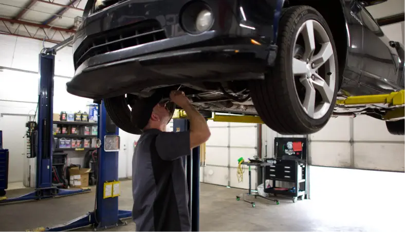 A mechanic at Miller Brothers Automotive performs detailed work underneath a car on a hydraulic lift, essential for pre-purchase & pre-trip inspections and other auto repair in Tecumseh, OK.