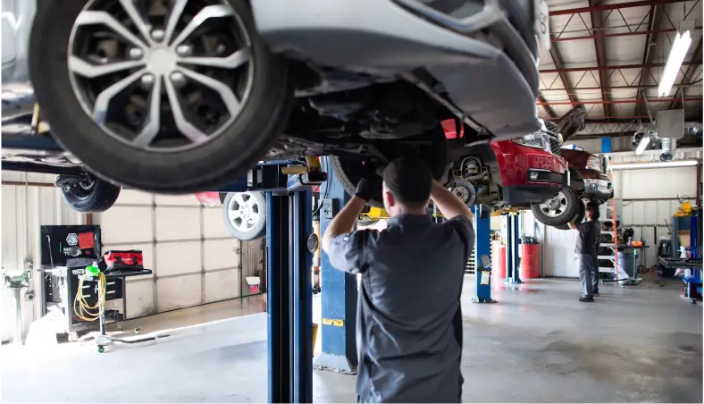 Inside Miller Brothers Automotive, a mechanic focuses on steering & suspension repair under a raised car, highlighting their expertise in auto repair in Tecumseh, OK.