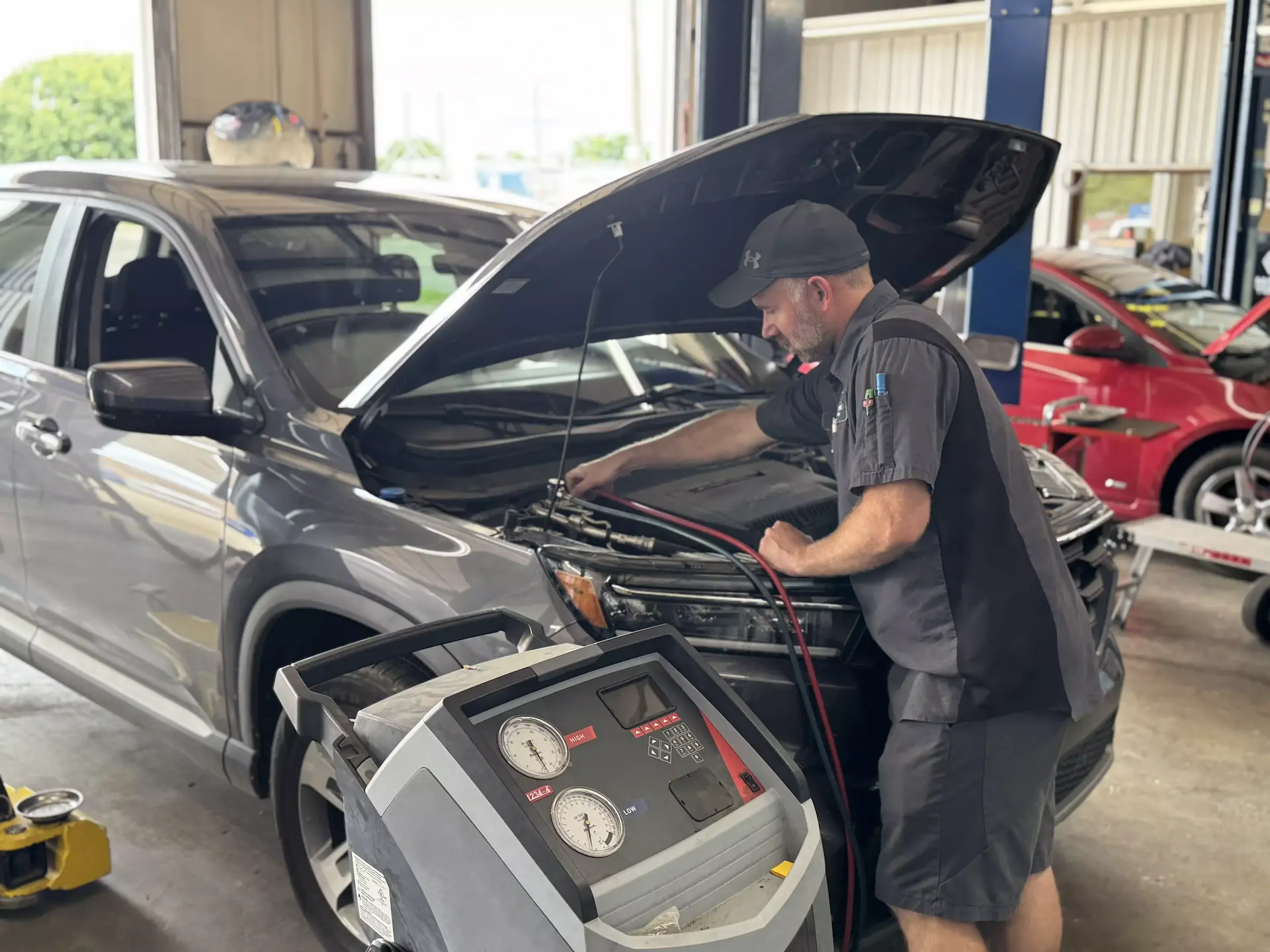 A technician at Miller Brothers Automotive servicing the air conditioning system of a gray SUV using a refrigerant recovery machine in a professional auto repair shop.