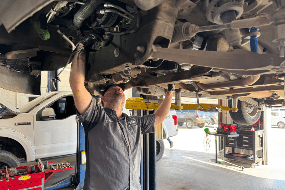 Cold weather car maintenance in Tecumseh, OK. Miller Brothers Automotive. A mechanic wearing gloves works on the front brake assembly of a red Chevrolet Tahoe lifted on a car hoist inside an auto repair shop.