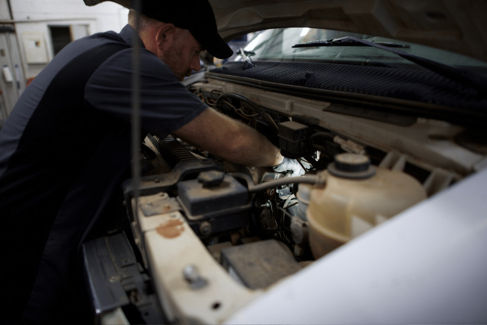 Auto Repair in Tecumseh, OK. Miller Brothers Automotive. A mechanic working under the hood of a car in an auto repair shop, focused on diagnosing or fixing the vehicle, with various tools and equipment in the background.