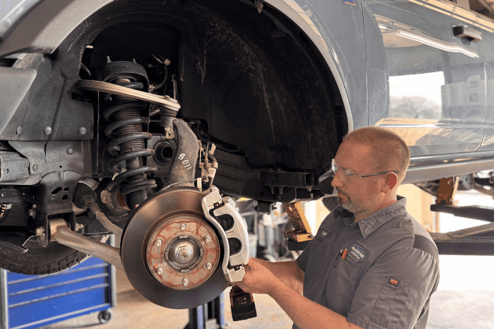 Brake repair near Tecumseh, OK by Miller Brothers Automotive. Image of a technician servicing a vehicle’s brake rotor and suspension components on a lift, highlighting precise brake diagnostics, suspension maintenance, and safe, reliable vehicle performance.